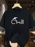 A black short-sleeve t-shirt hanging on a wooden hanger, featuring a white graphic of the word 'CHILL' with a beach umbrella and lounge chair, and a small yellow star. A hand is holding the bottom of the shirt in a cafe setting.