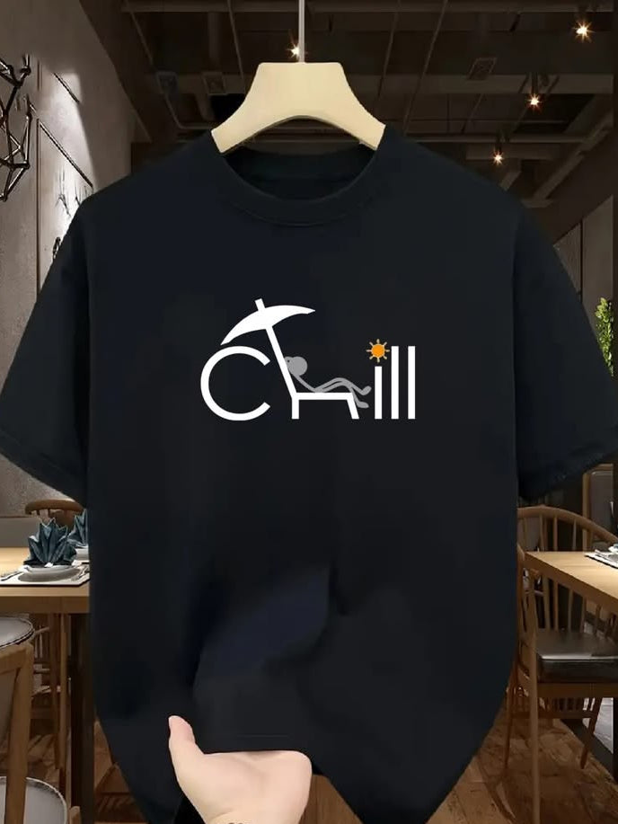 A black short-sleeve t-shirt hanging on a wooden hanger, featuring a white graphic of the word 'CHILL' with a beach umbrella and lounge chair, and a small yellow star. A hand is holding the bottom of the shirt in a cafe setting.